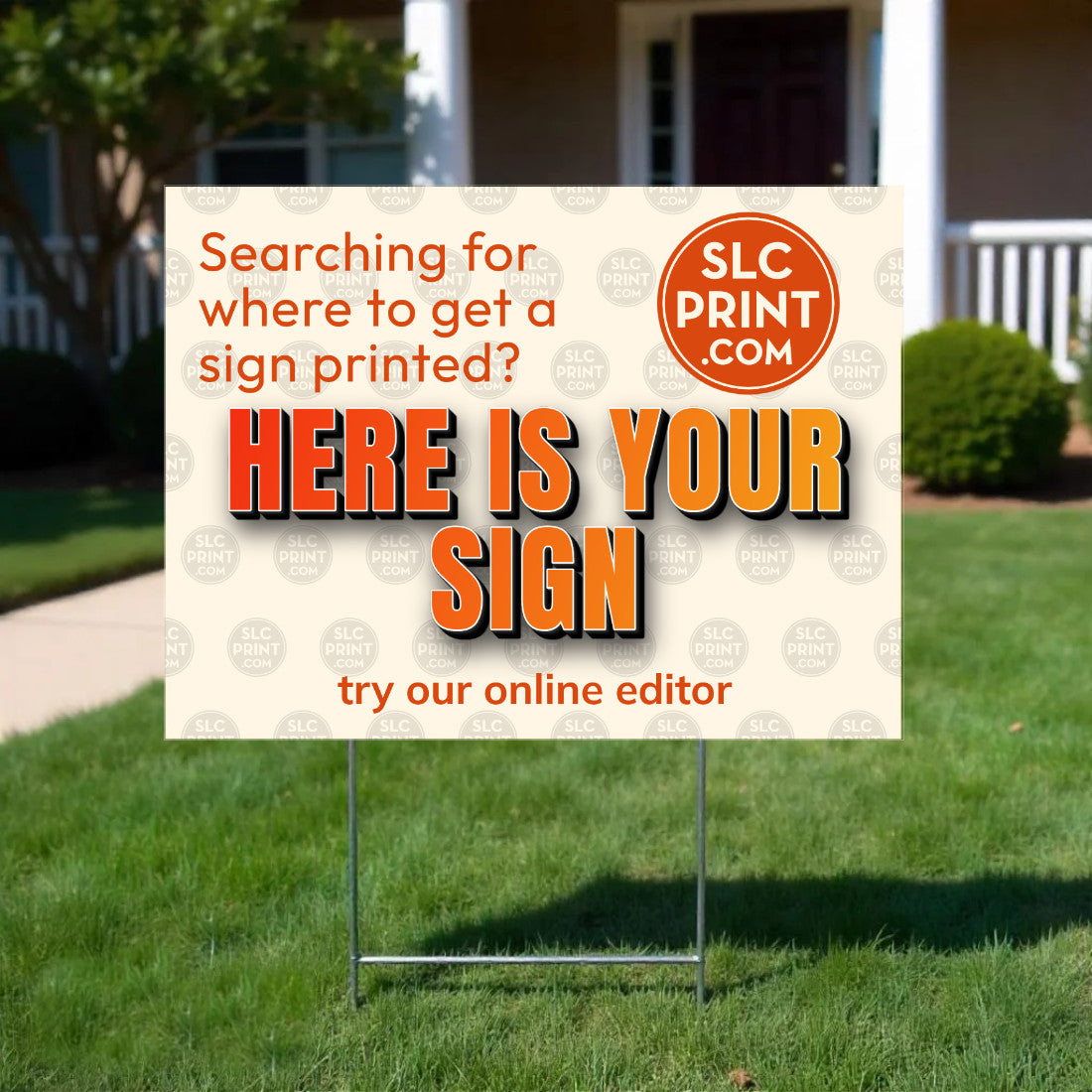 A yard sign displayed on a green lawn in front of a house. The sign has a cream background with orange and black text reading 'Here is your sign' and a circular 'SLC Print .
